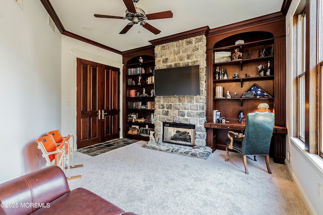 interior space featuring built in shelves, crown molding, carpet floors, ceiling fan, and a fireplace