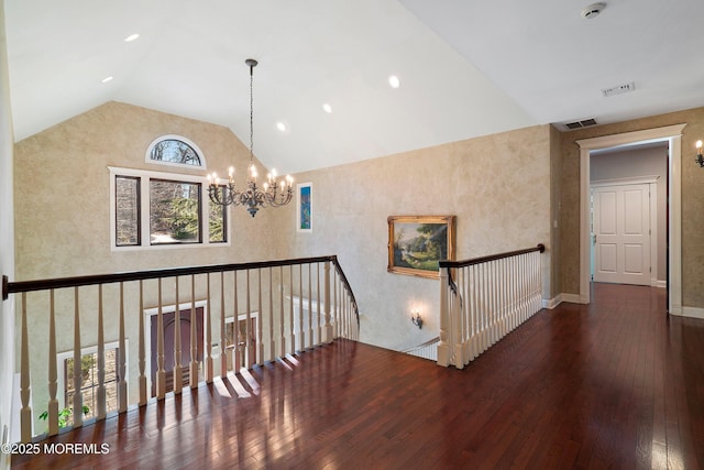 hall with dark wood-type flooring, a chandelier, and high vaulted ceiling