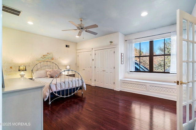 bedroom with ceiling fan, dark hardwood / wood-style flooring, and two closets