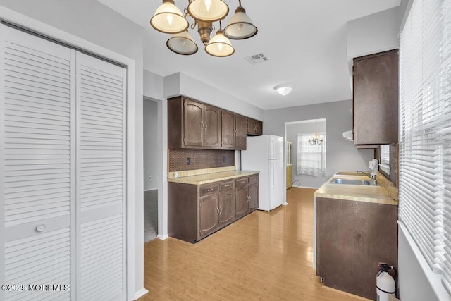 kitchen featuring sink, backsplash, hanging light fixtures, dark brown cabinets, and a chandelier