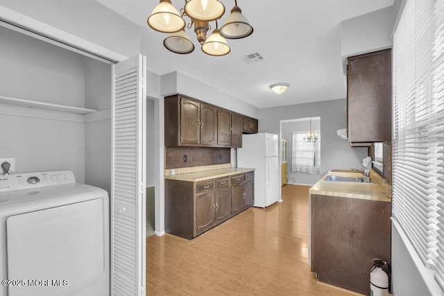 kitchen featuring dark brown cabinetry, sink, an inviting chandelier, white fridge, and washer / clothes dryer