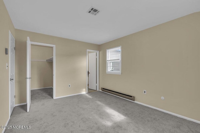 unfurnished bedroom with a walk in closet, light colored carpet, baseboard heating, and a closet