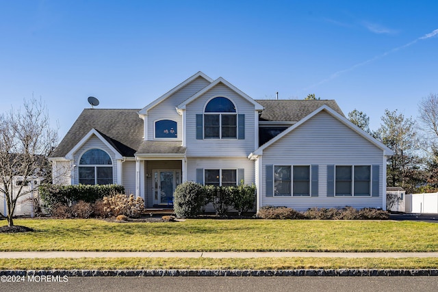 traditional-style home featuring a front lawn, fence, and roof with shingles