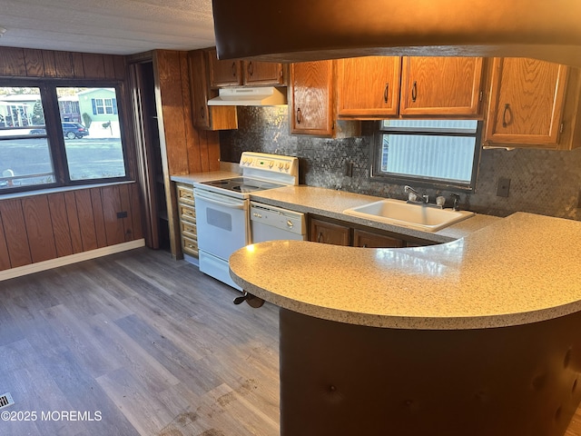 kitchen featuring dark wood-type flooring, sink, wooden walls, white appliances, and decorative backsplash