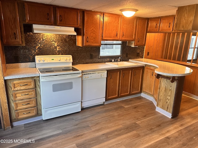 kitchen with hardwood / wood-style floors, range hood, sink, kitchen peninsula, and white appliances