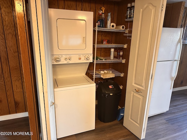 washroom with stacked washer and clothes dryer, dark hardwood / wood-style flooring, and wood walls