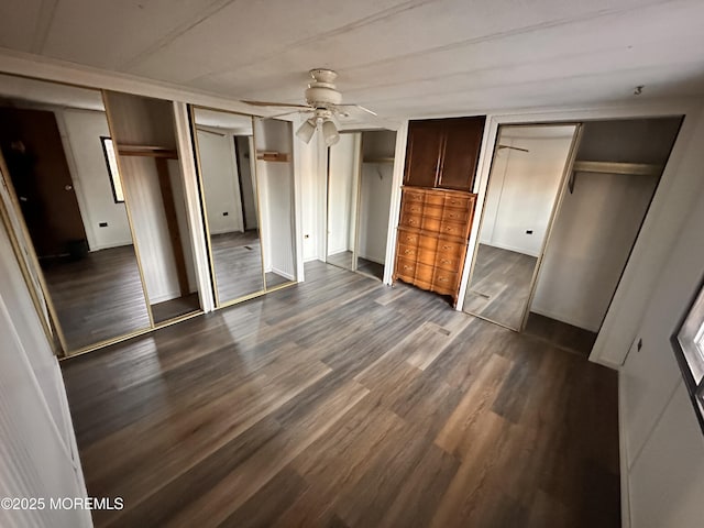 unfurnished bedroom with dark wood-type flooring, ceiling fan, and two closets