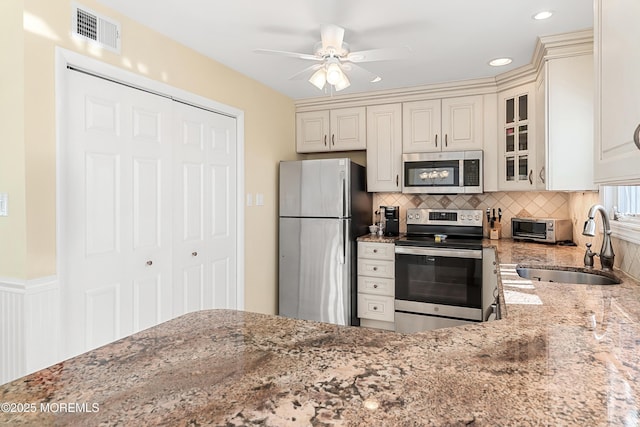 kitchen featuring sink, light stone counters, tasteful backsplash, ceiling fan, and stainless steel appliances