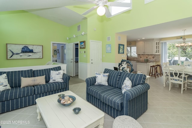 living room featuring a high ceiling, light tile patterned flooring, and ceiling fan with notable chandelier