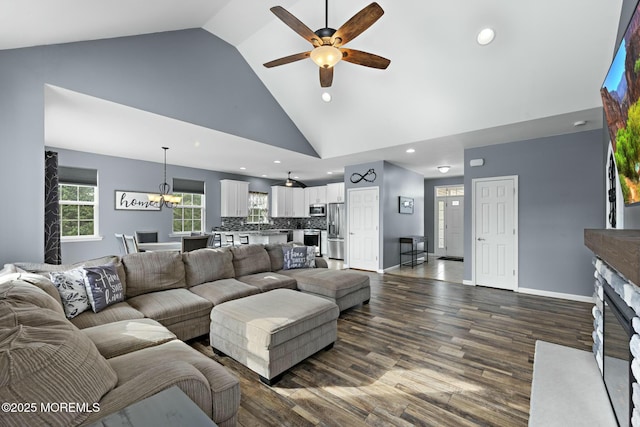 living room with ceiling fan with notable chandelier, a fireplace, dark hardwood / wood-style floors, and high vaulted ceiling