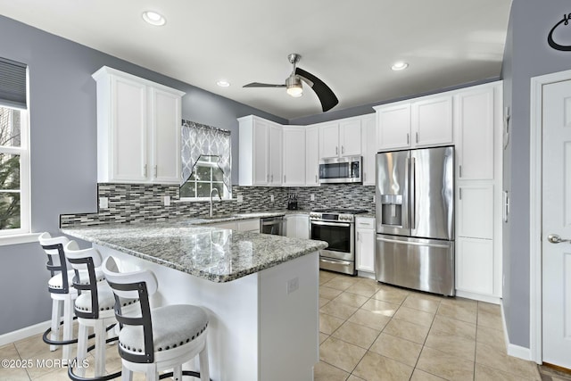 kitchen with light tile patterned flooring, sink, white cabinetry, kitchen peninsula, and stainless steel appliances