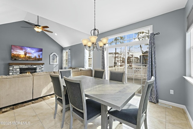 dining space with light tile patterned floors, ceiling fan with notable chandelier, a fireplace, and vaulted ceiling