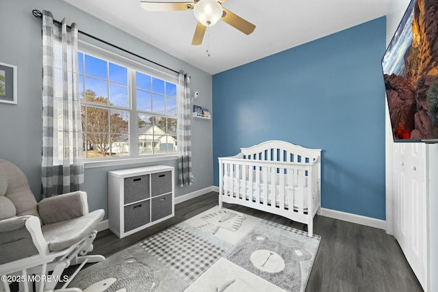 bedroom featuring dark wood-type flooring, a crib, and ceiling fan