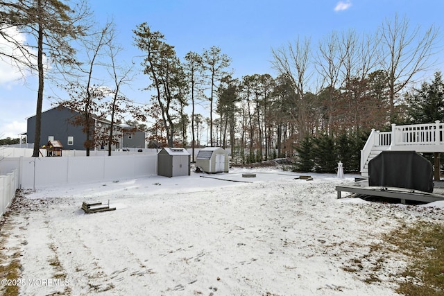 snowy yard with a storage shed and a deck