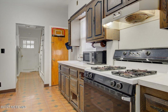 kitchen with light tile patterned flooring, white gas range, dark brown cabinets, and sink