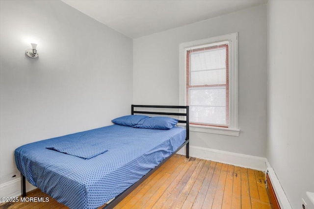 bedroom with hardwood / wood-style flooring, baseboard heating, and multiple windows