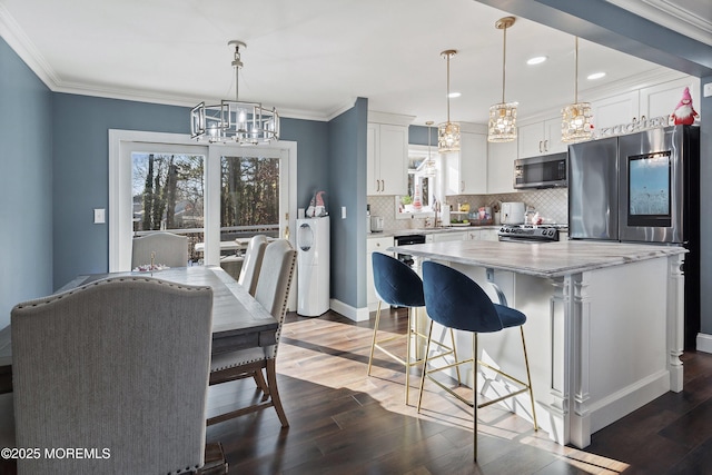 kitchen with hanging light fixtures, white cabinetry, appliances with stainless steel finishes, and light stone counters