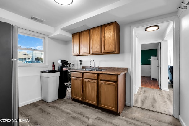 kitchen featuring brown cabinetry, light wood-type flooring, a sink, and visible vents