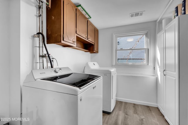 washroom featuring washer and clothes dryer, visible vents, cabinet space, light wood-style flooring, and baseboards