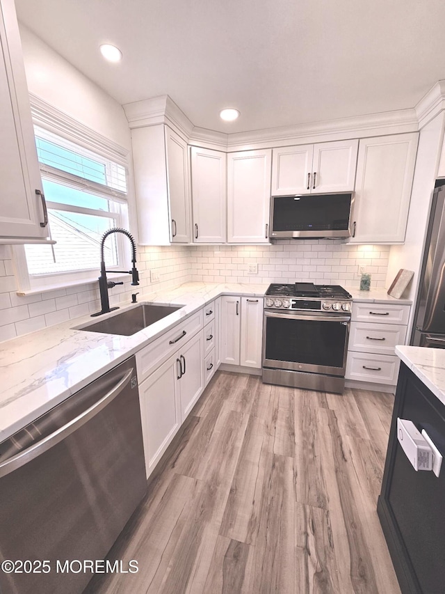 kitchen with light stone counters, white cabinetry, stainless steel appliances, and a sink