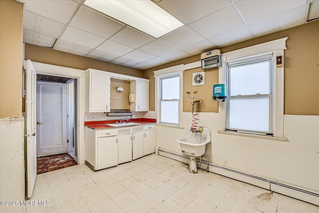 kitchen featuring a baseboard radiator, a drop ceiling, sink, and white cabinets