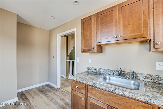 kitchen with light hardwood / wood-style floors, light stone countertops, and sink