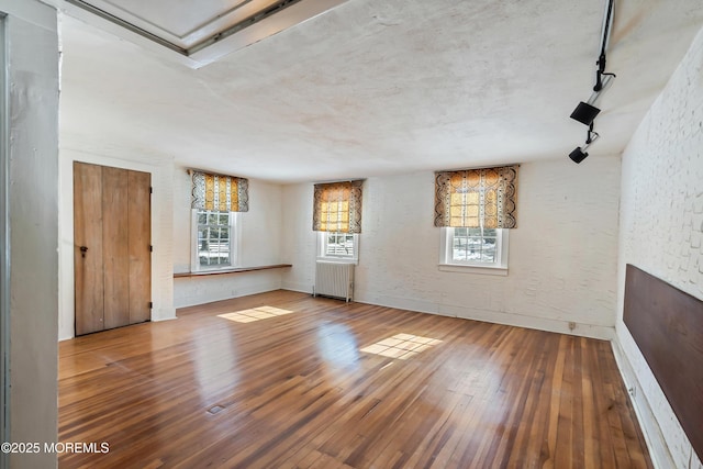 unfurnished living room featuring rail lighting, radiator, and hardwood / wood-style floors