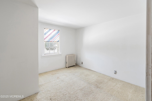 spare room featuring light carpet and radiator