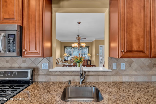 kitchen with sink, ornamental molding, a notable chandelier, light stone counters, and stainless steel appliances