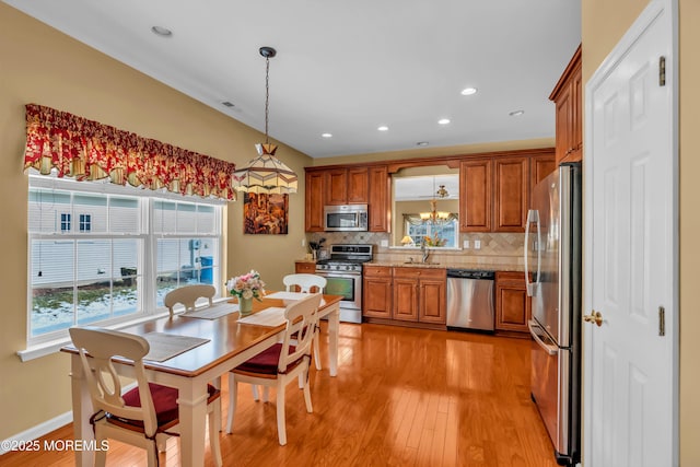 kitchen with appliances with stainless steel finishes, sink, decorative backsplash, hanging light fixtures, and light hardwood / wood-style floors