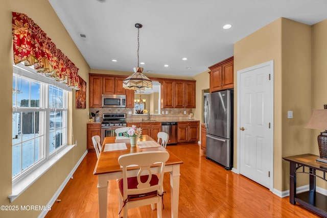 kitchen with appliances with stainless steel finishes, sink, decorative backsplash, hanging light fixtures, and light hardwood / wood-style floors