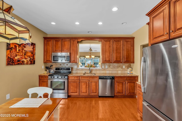 kitchen with appliances with stainless steel finishes, sink, decorative backsplash, light stone counters, and light hardwood / wood-style flooring