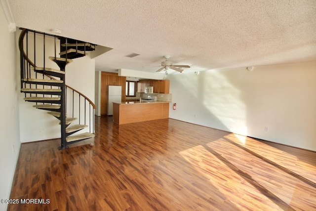 unfurnished living room featuring dark wood-type flooring, ceiling fan, and a textured ceiling