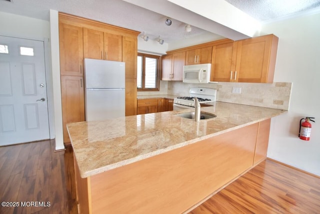 kitchen featuring wood-type flooring, light stone counters, white appliances, and kitchen peninsula