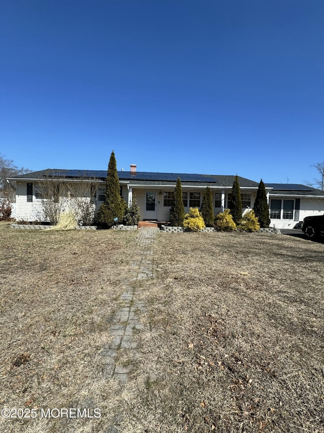 view of front of home with roof mounted solar panels and a chimney