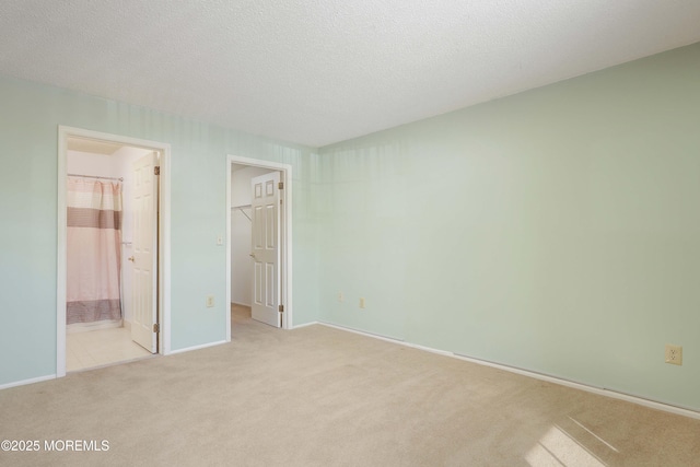 unfurnished bedroom with connected bathroom, a textured ceiling, light carpet, a walk in closet, and a closet