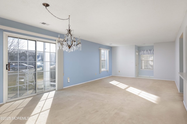 carpeted spare room featuring a healthy amount of sunlight and a notable chandelier