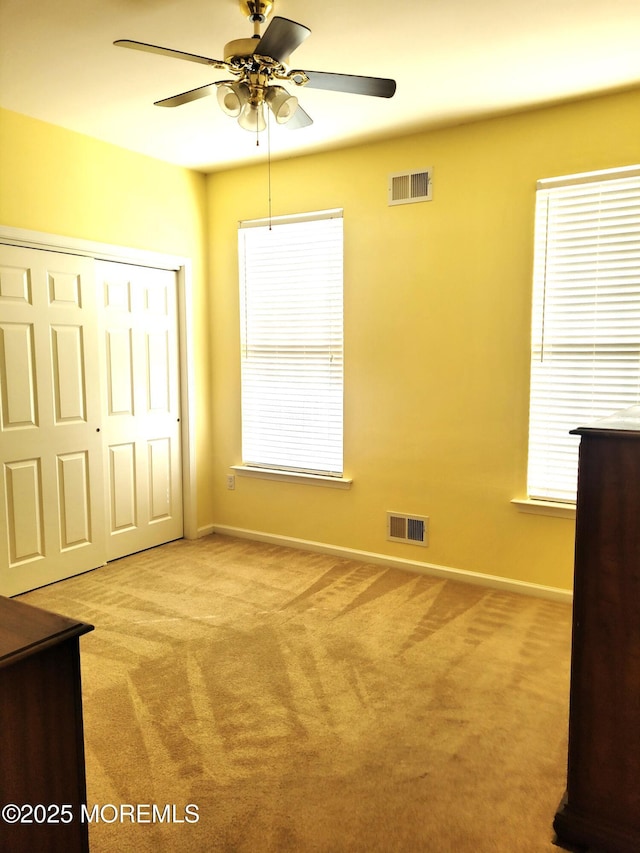 unfurnished bedroom featuring ceiling fan, light colored carpet, and a closet