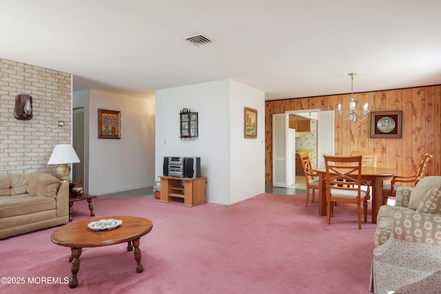 carpeted living room with a notable chandelier and wood walls