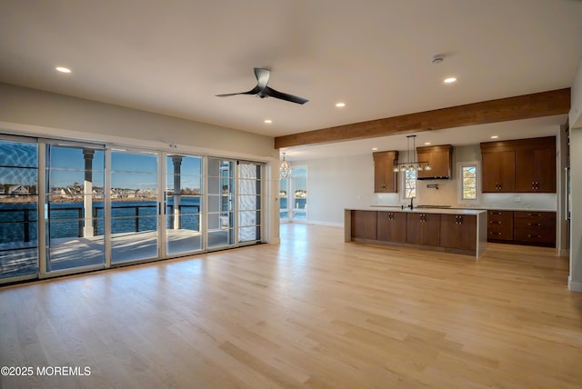 unfurnished living room featuring sink, light hardwood / wood-style flooring, ceiling fan, beam ceiling, and a water view