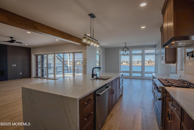 kitchen featuring appliances with stainless steel finishes, decorative light fixtures, sink, light stone counters, and a center island with sink