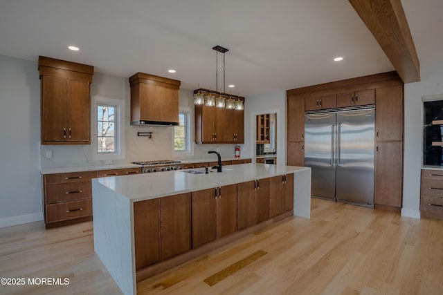 kitchen with sink, light hardwood / wood-style flooring, appliances with stainless steel finishes, a kitchen island with sink, and hanging light fixtures