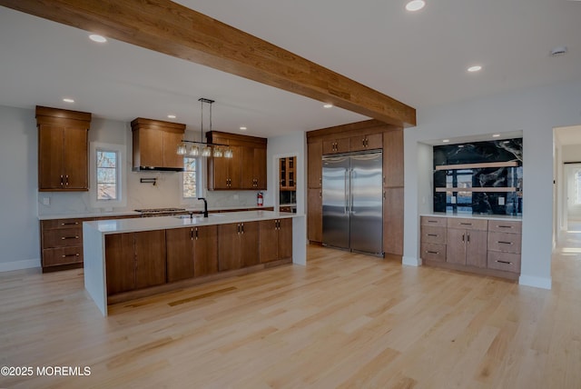 kitchen with light hardwood / wood-style flooring, appliances with stainless steel finishes, a center island with sink, decorative light fixtures, and beamed ceiling