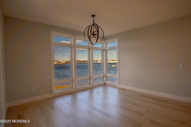 unfurnished room featuring light wood-type flooring, a chandelier, and a water view