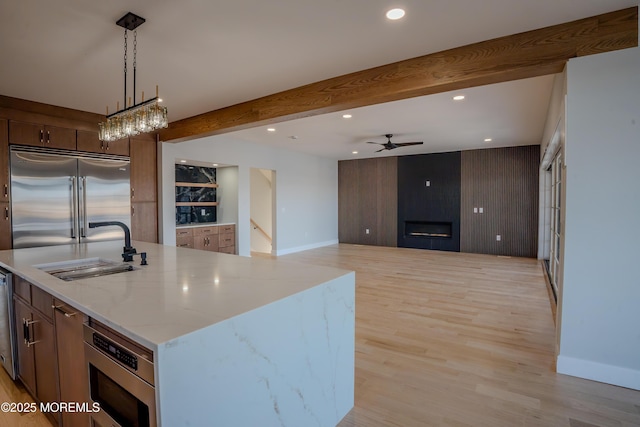 kitchen with sink, built in appliances, pendant lighting, light stone countertops, and a kitchen island with sink