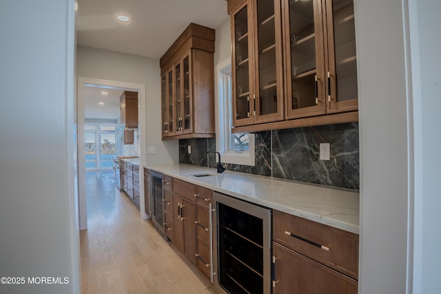 kitchen featuring sink, backsplash, light hardwood / wood-style floors, light stone countertops, and beverage cooler