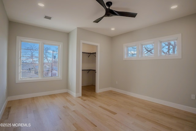 unfurnished bedroom featuring ceiling fan, a walk in closet, light hardwood / wood-style floors, and a closet