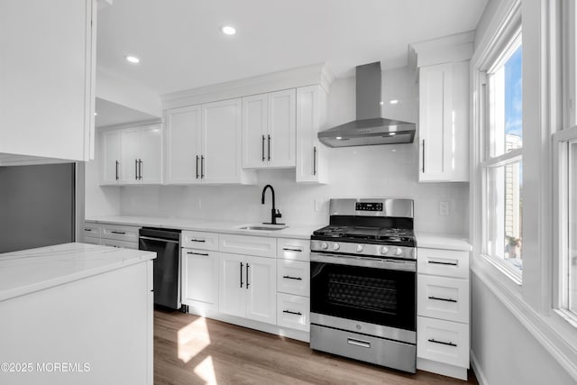 kitchen with sink, stainless steel gas range oven, white cabinetry, a healthy amount of sunlight, and wall chimney range hood