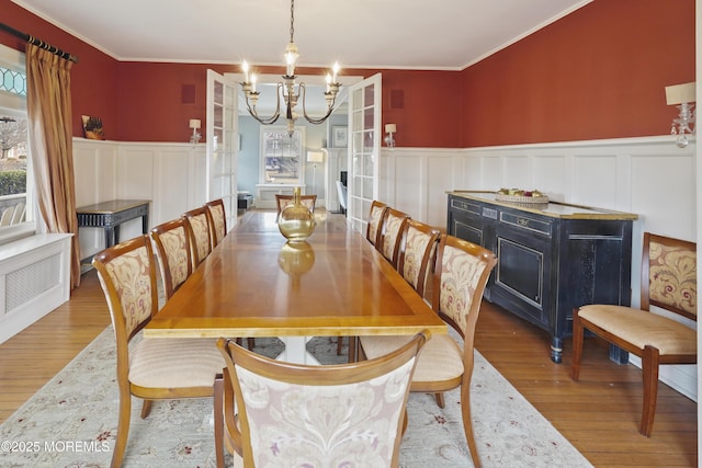 dining room with crown molding, an inviting chandelier, light hardwood / wood-style floors, and french doors