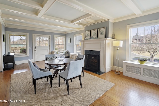 dining room featuring radiator, crown molding, beamed ceiling, and light wood-type flooring